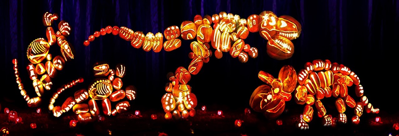 Glowing dinosaur scene built from carved pumpkins